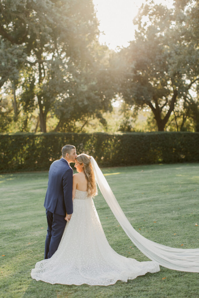 Bride and groom sharing a tender moment during golden hour in a scenic outdoor setting, bathed in warm, soft sunlight.