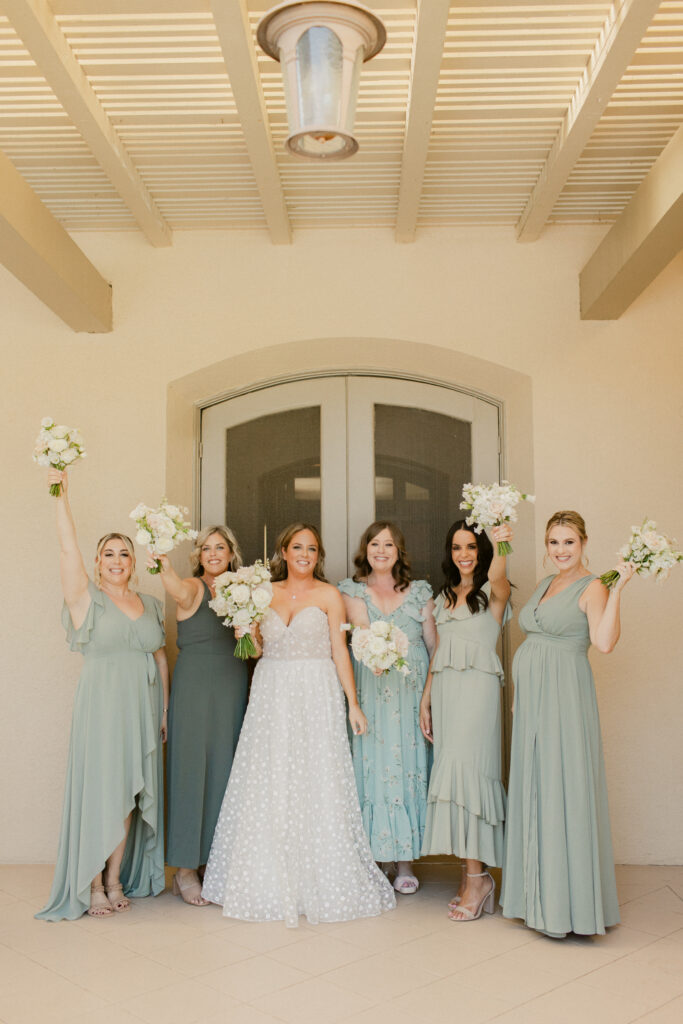 Bride in a stunning white gown, surrounded by her bridesmaids in sage green dresses, posing for a group photo with a scenic Morgan Hill backdrop.