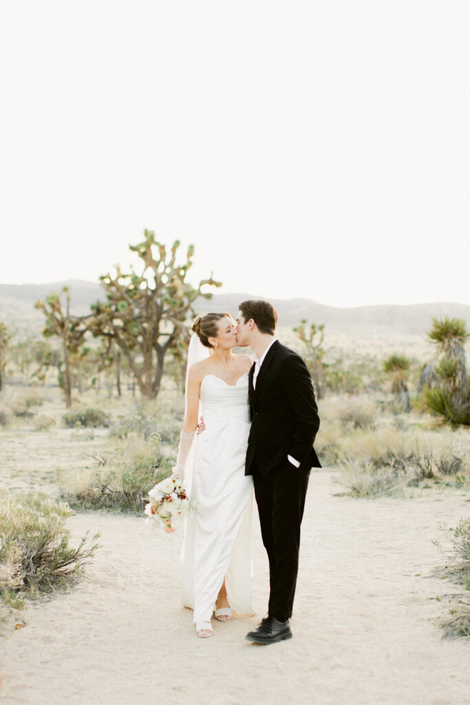 Bride and groom share a romantic kiss in the Joshua Tree desert at sunset