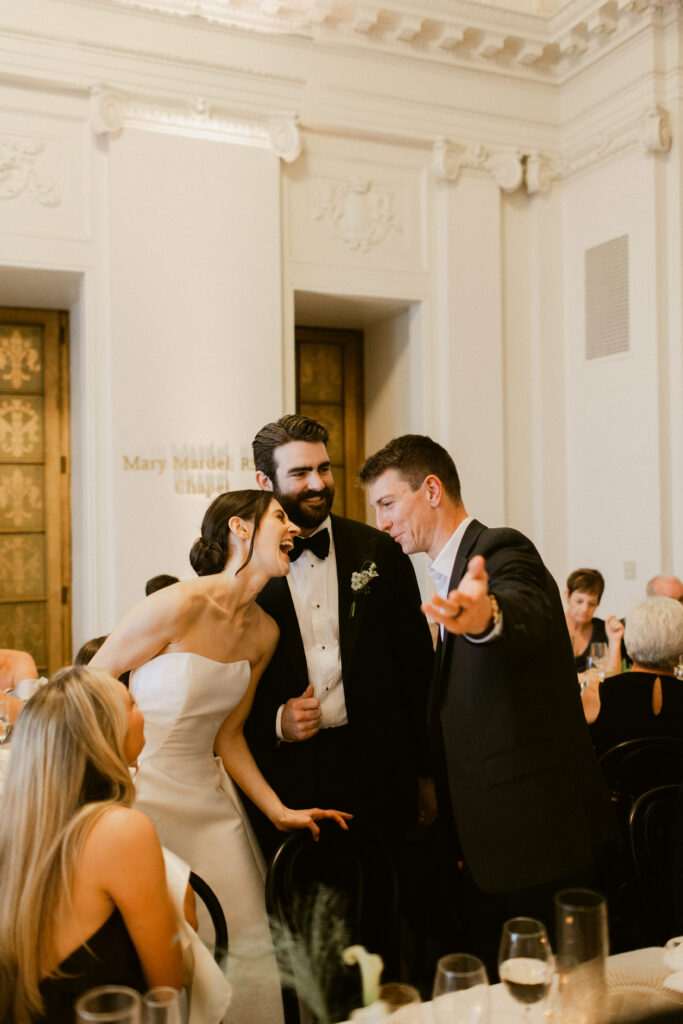 Bride and groom laughing with guest during wedding reception